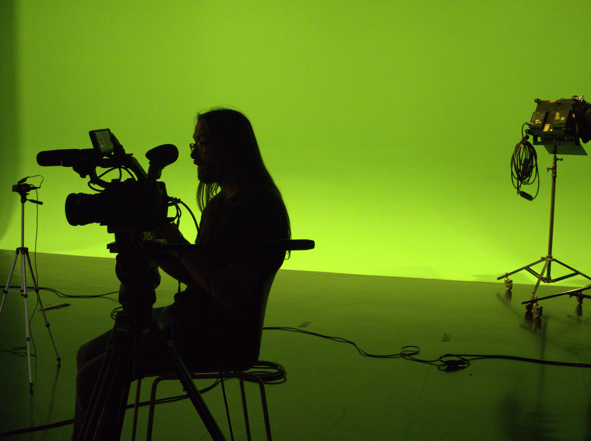 Camera Operator sitting at camera with a green and black background